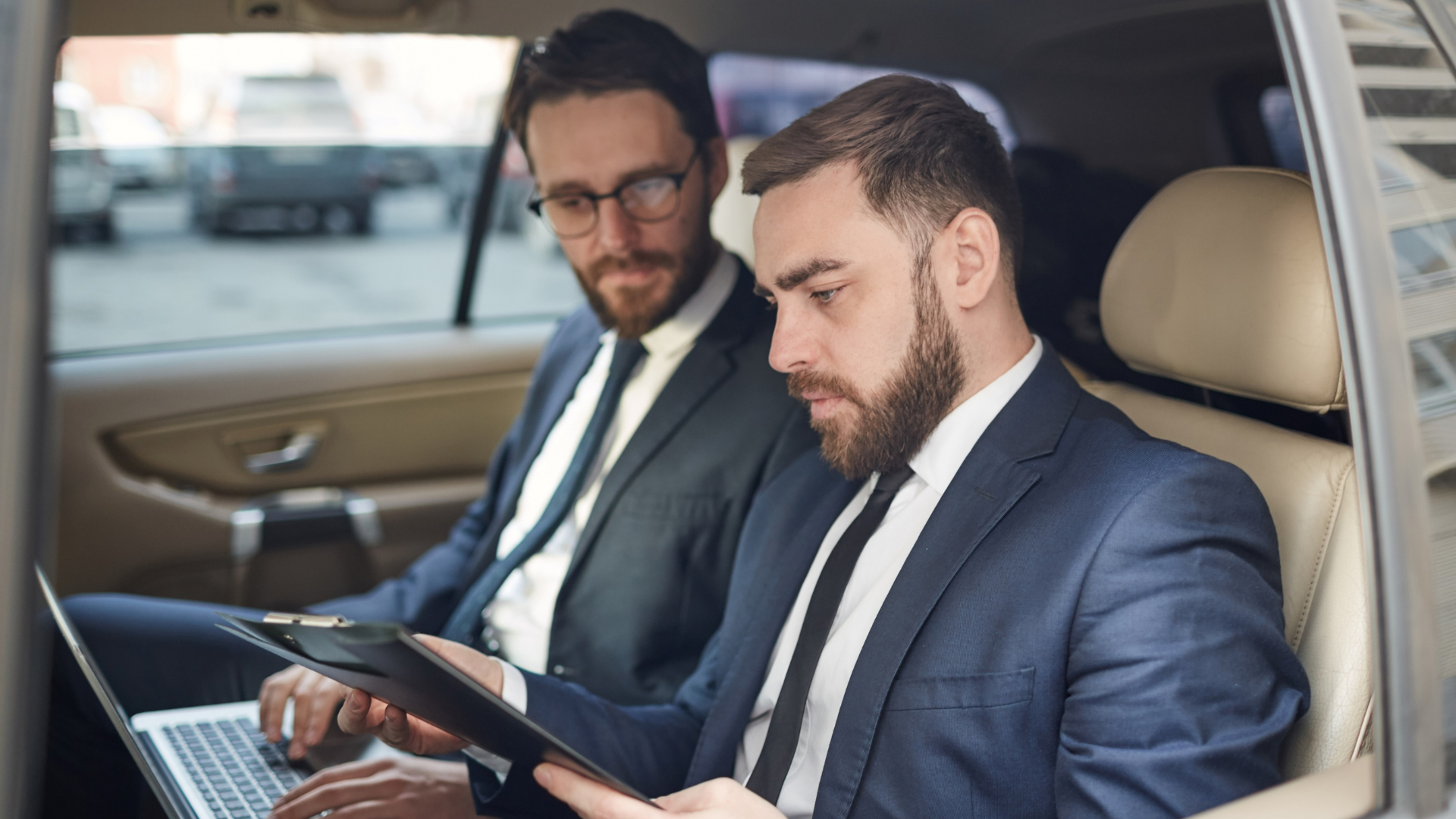 Two business colleagues reviewing documents in the back seat of a car