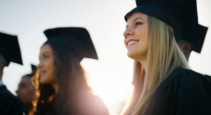 Smiling graduate in cap and gown at sunset