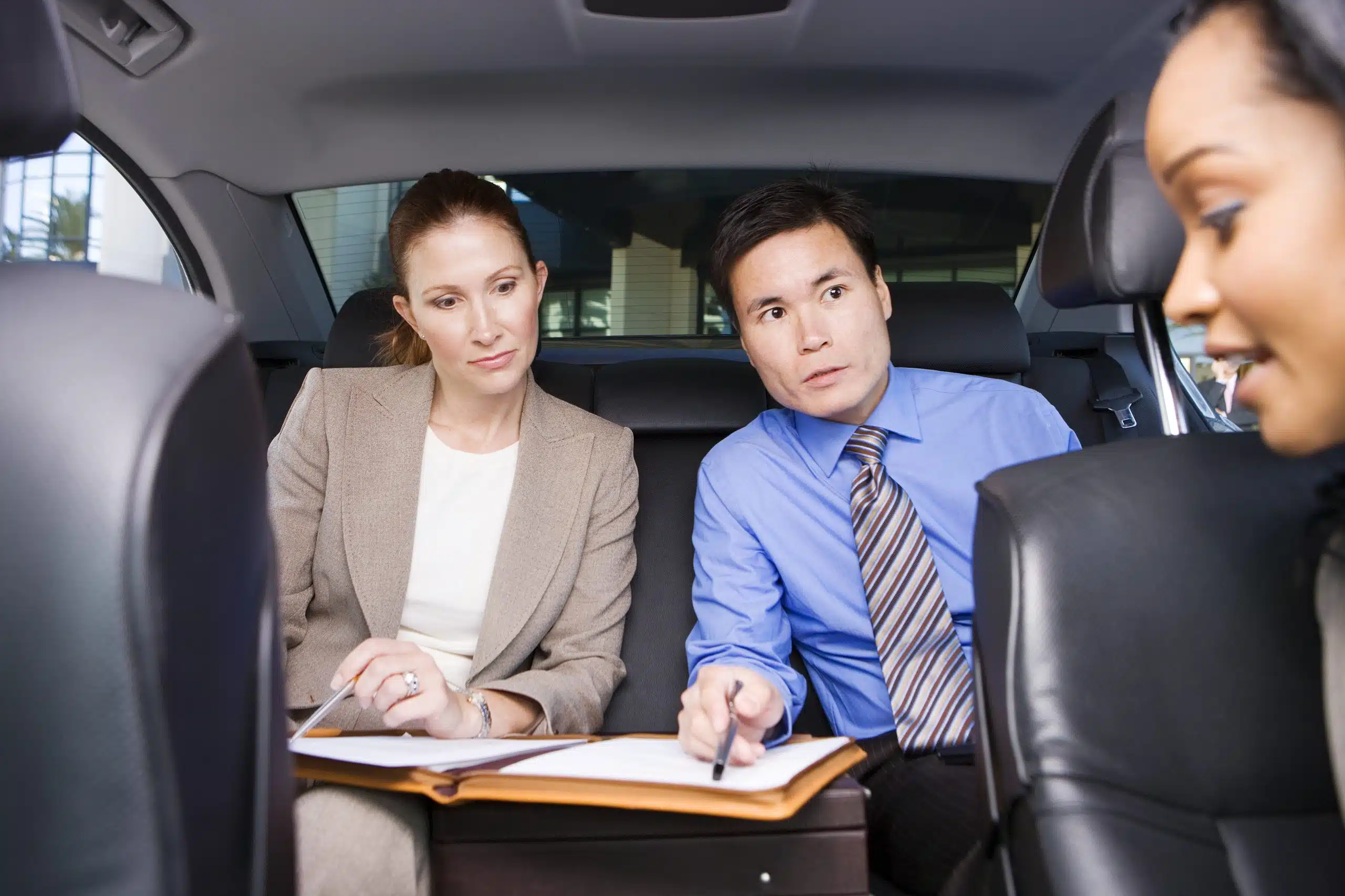 Business colleagues reviewing documents in the back seat of a car