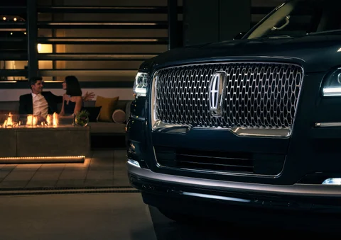 Close-up of a Lincoln Navigator grille with a couple relaxing by a fire pit at night